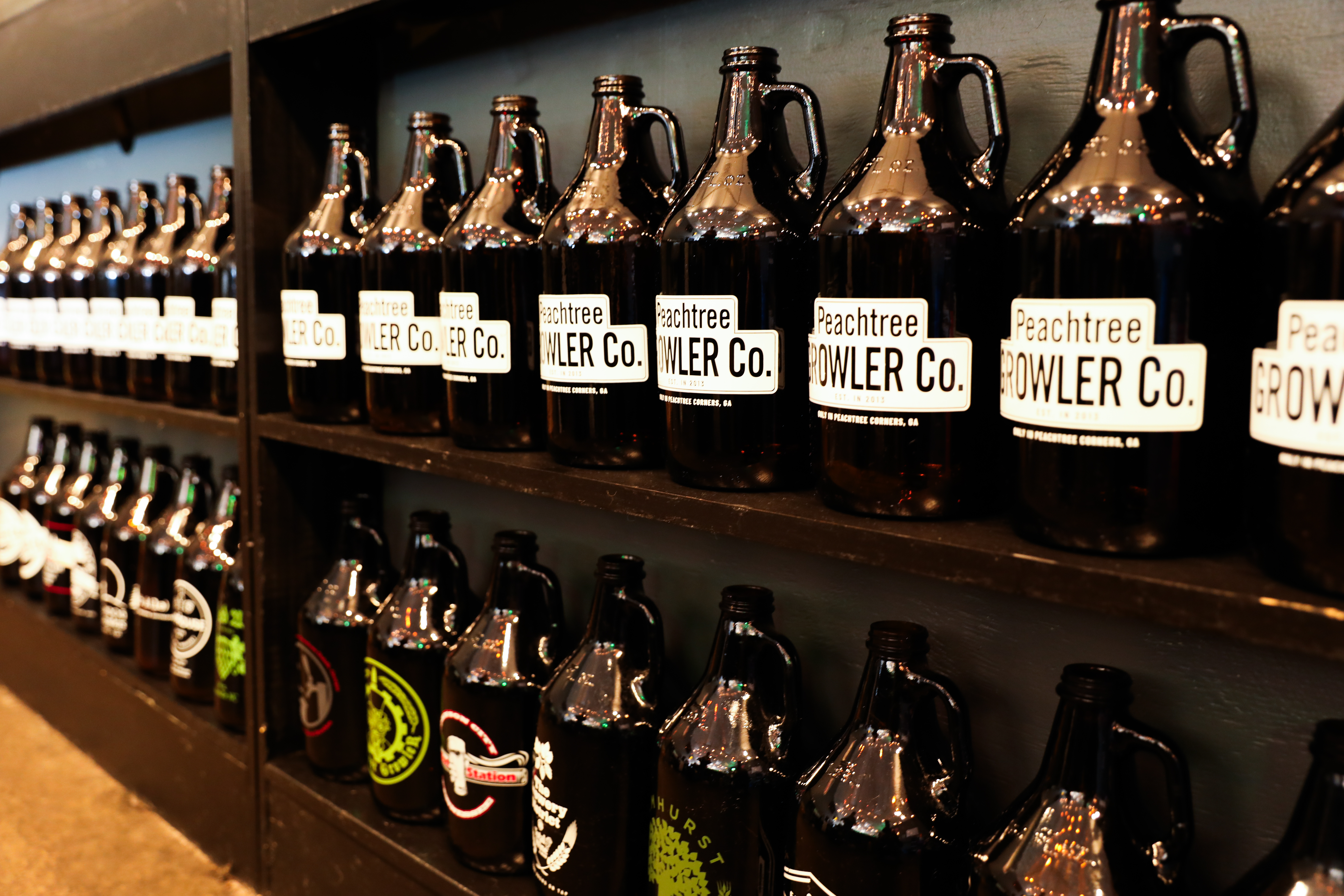 two shelves lined with glass growlers with Peachtree Growler labels in white.